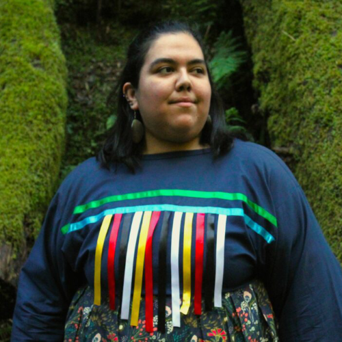 Lindsey posing in front of a mossy background, wearing colorful dress