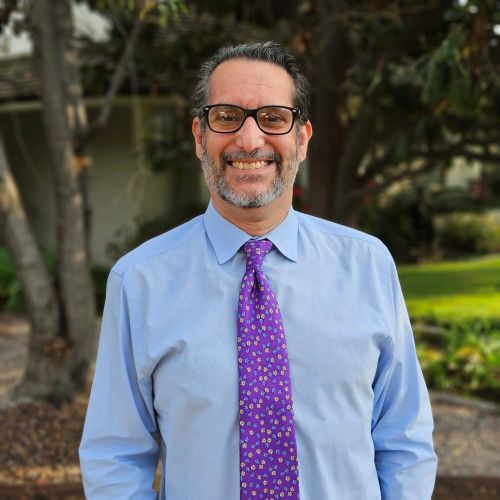 Photo of a man wearing a blue shirt and purple tie, smiling