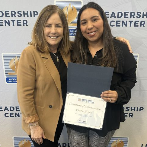 Two women posing together, one of them holding up a certificate